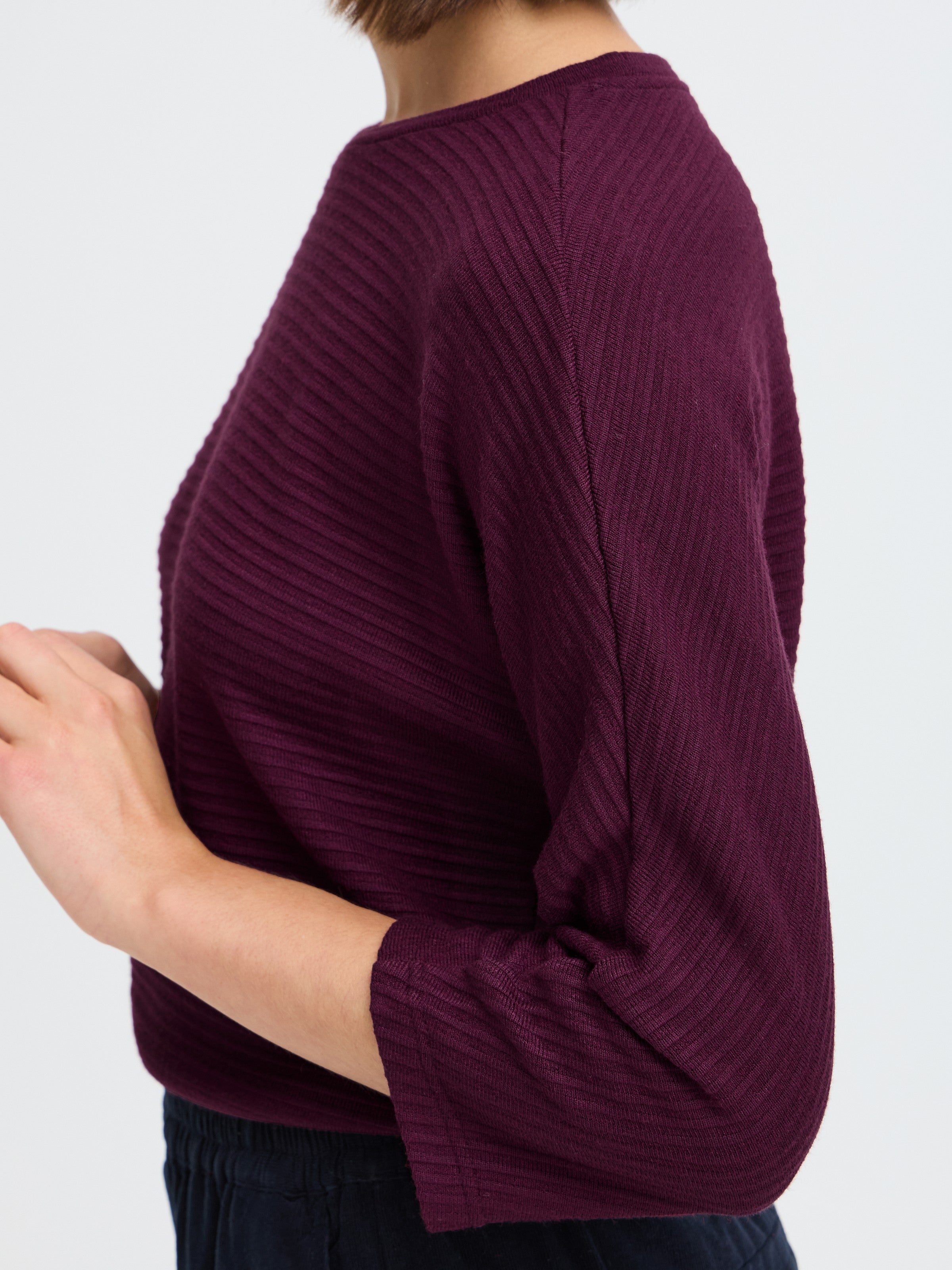 Close-up of a ribbed, plum-colored sweater with three-quarter sleeves on a light background.