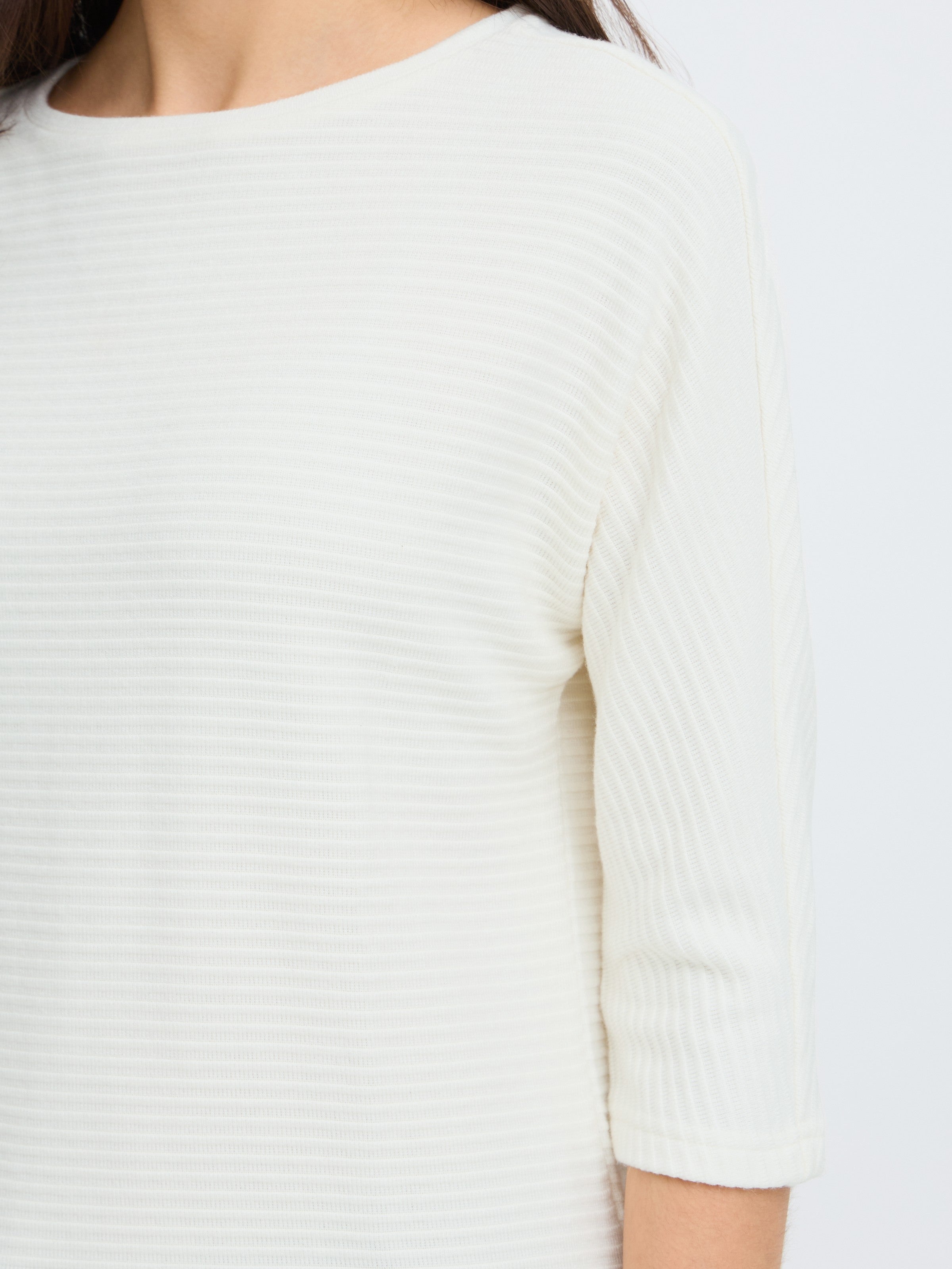 Close-up of an off-white textured top with three-quarter sleeves and subtle horizontal ribbing detail.