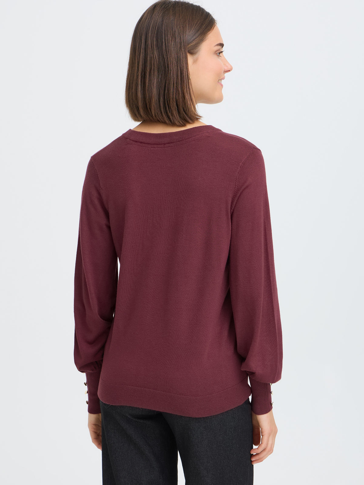 Back view of a burgundy long-sleeve sweater with cuff button details paired with dark pants against a plain background.