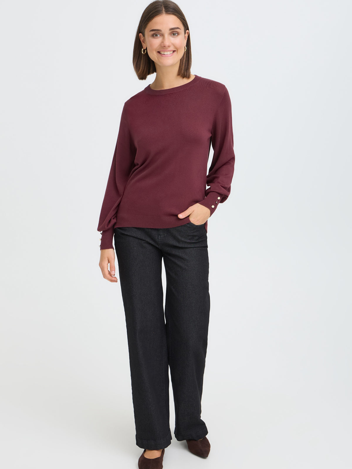 Long-sleeve burgundy sweater with button details on cuff paired with black wide-leg trousers and brown shoes.