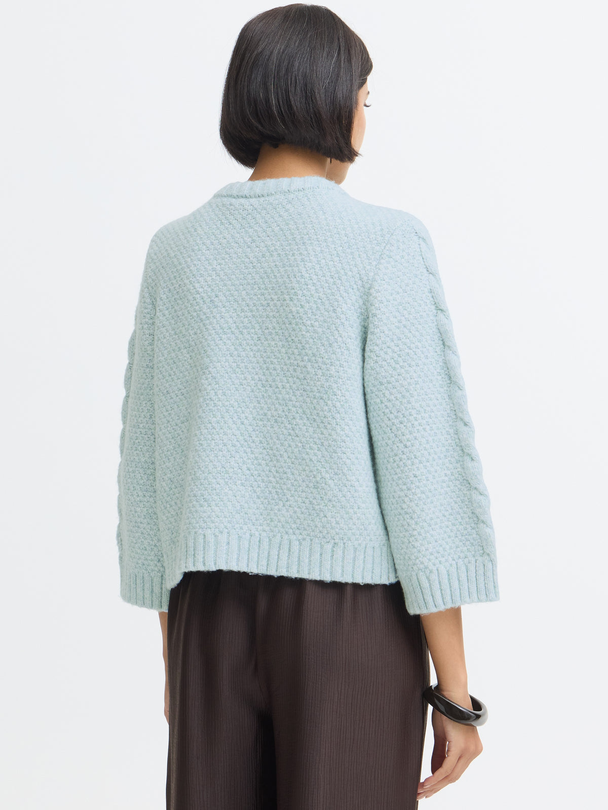 Light blue textured knit sweater shown from the back with braided sleeve details and a ribbed hem