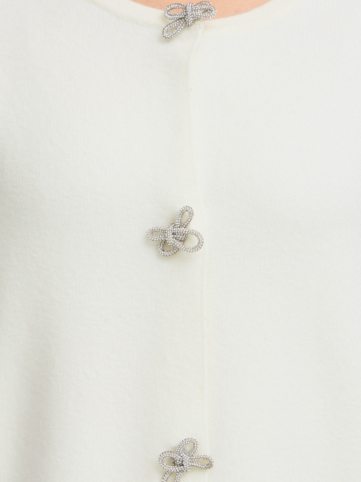 Close-up of a white knit cardigan with sparkling bow-shaped closures