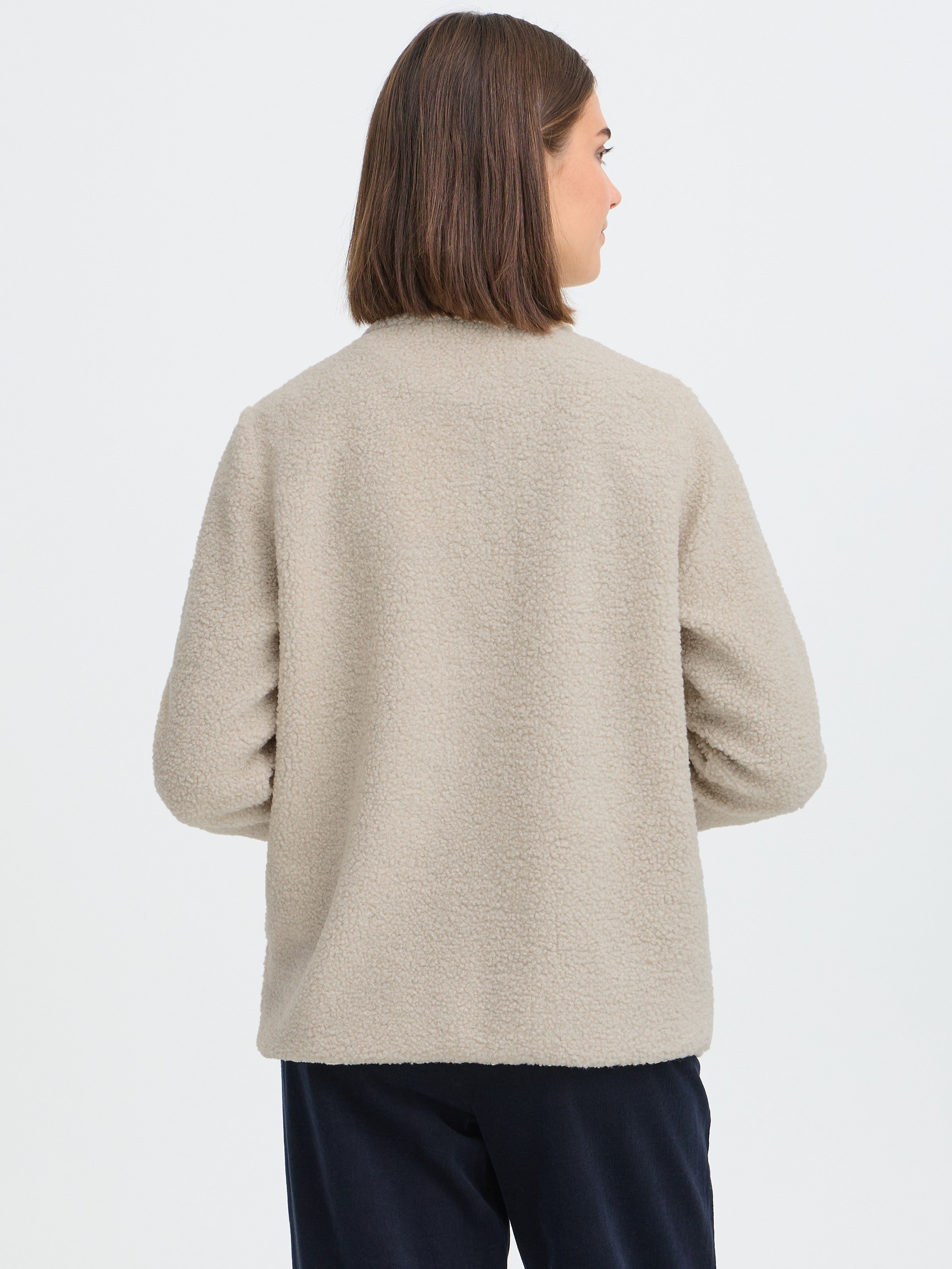 Back view of a beige textured fleece jacket paired with dark pants on a white background.