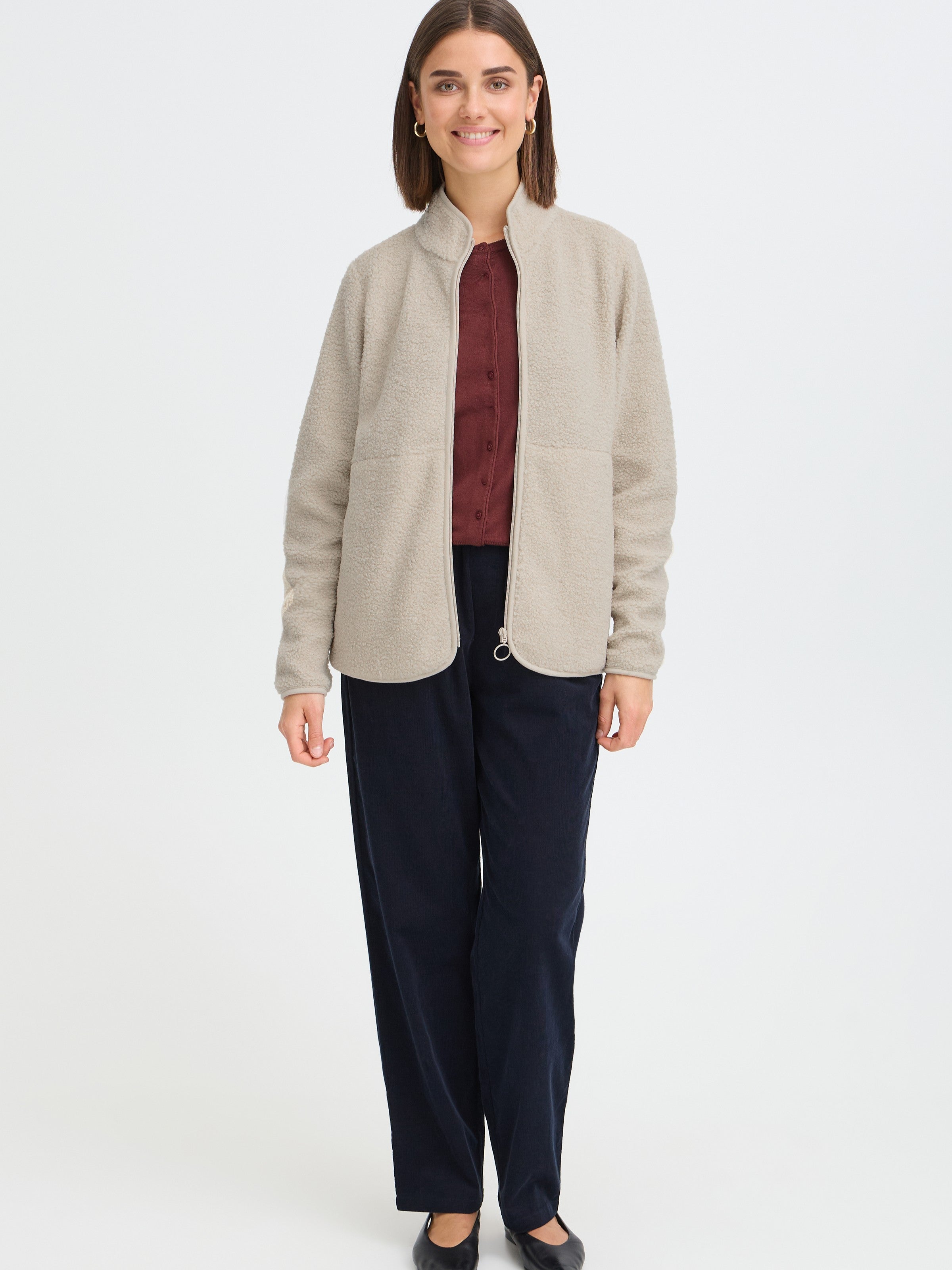 Light beige zip-up fleece jacket paired with a burgundy button-up top and black loose trousers.