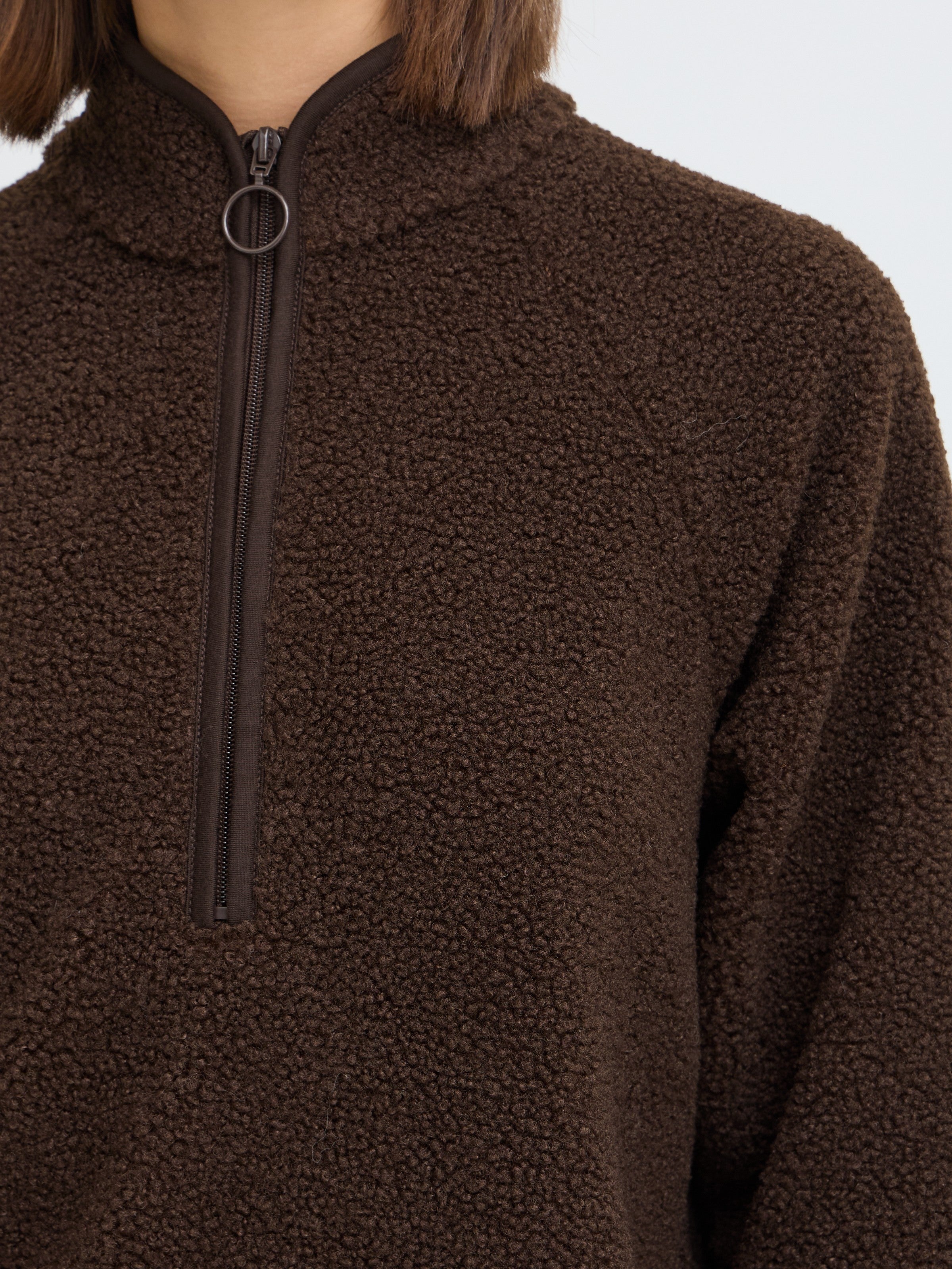 Close-up of a brown textured fleece jacket with a quarter-zip collar and a circular zipper pull