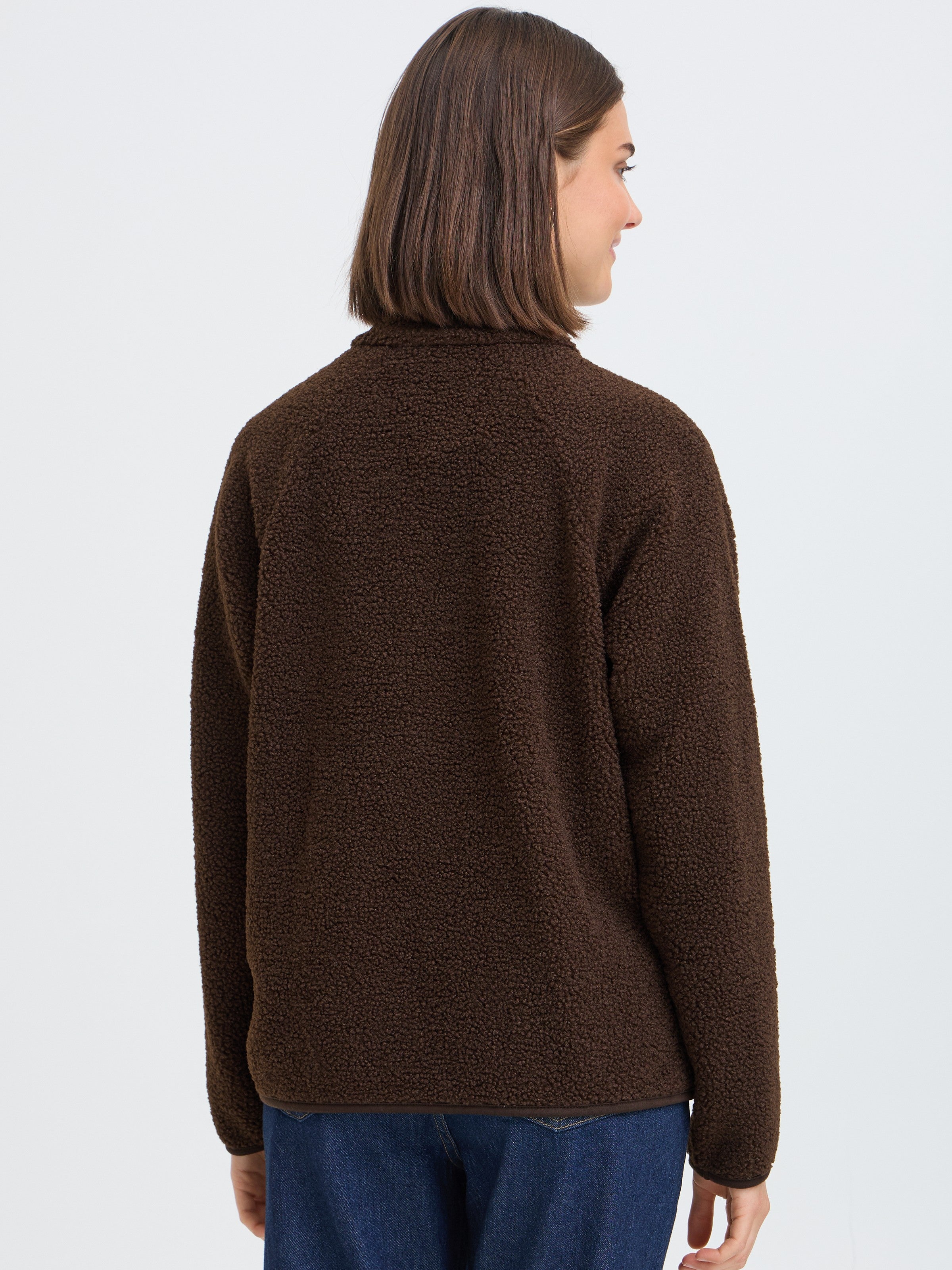 Back view of a dark brown textured fleece jacket paired with blue denim jeans on a neutral background.