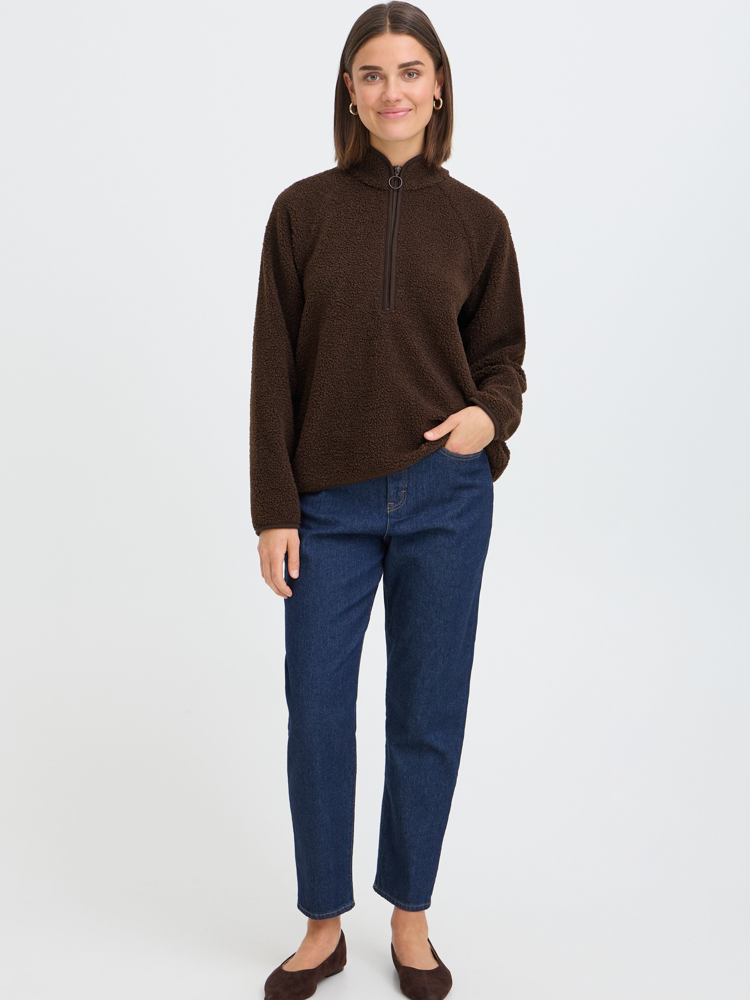 Brown quarter-zip fleece sweater paired with dark blue denim jeans and brown flat shoes on a plain background