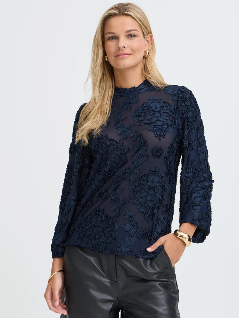 Blonde model with a navy textured long-sleeve top and black trousers