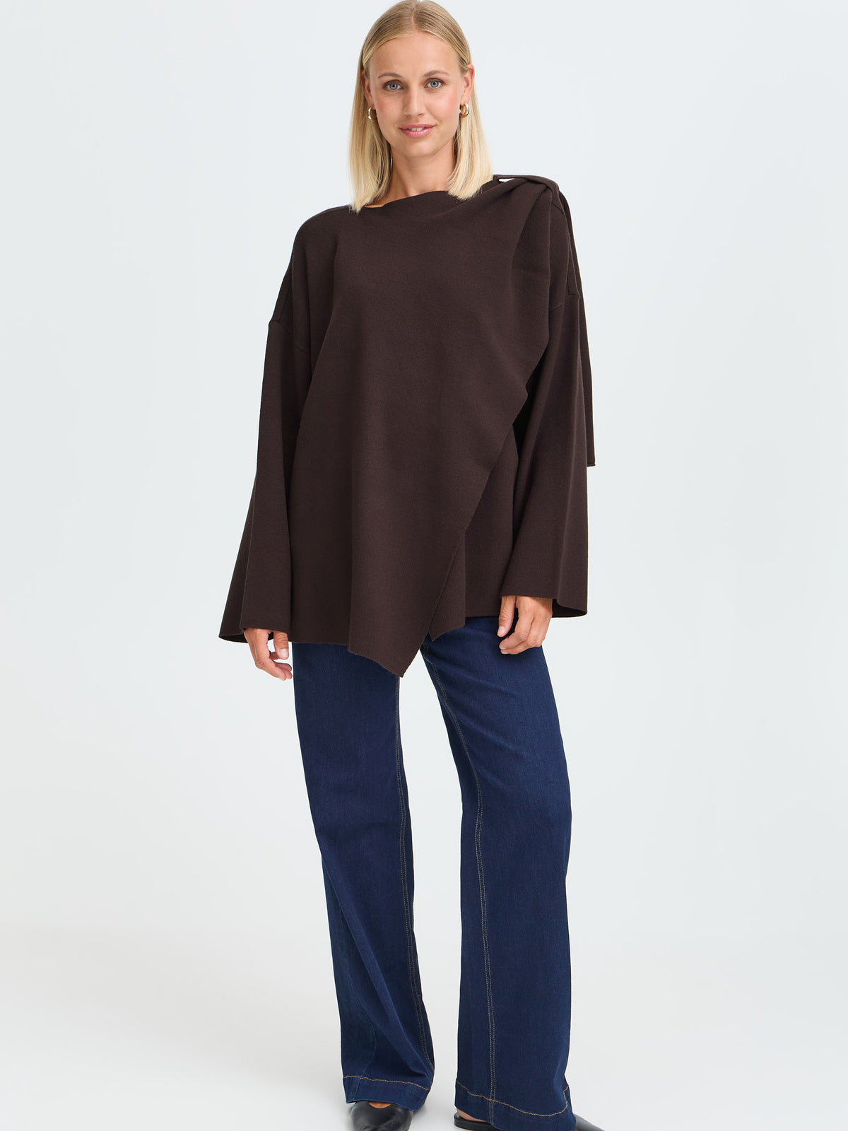 Blonde model in a dark brown oversized poncho top and wide-leg dark blue jeans