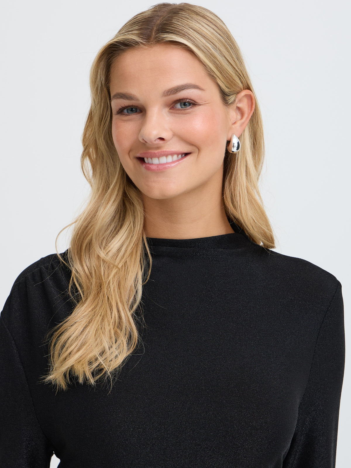 Smiling blonde with long hair and silver earrings in a black long-sleeve top