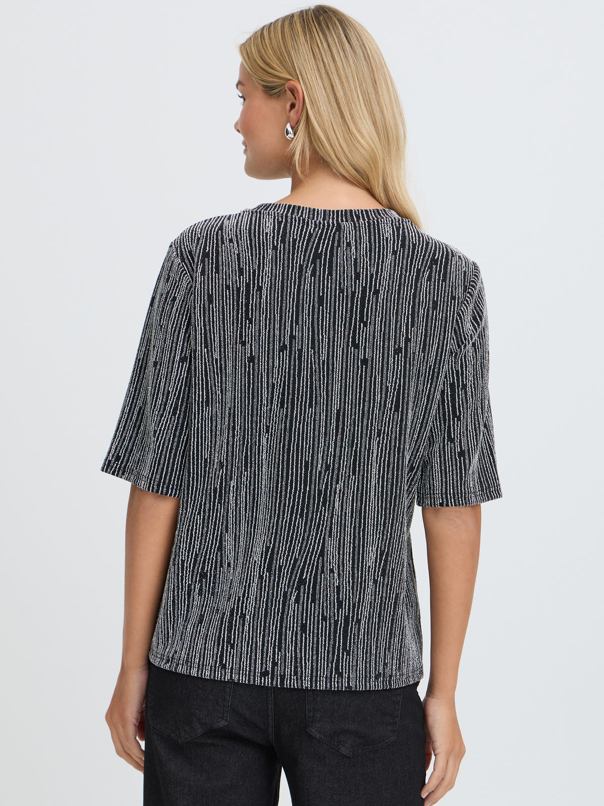 Back view of a blonde model in a black and white striped short sleeve top and dark trousers