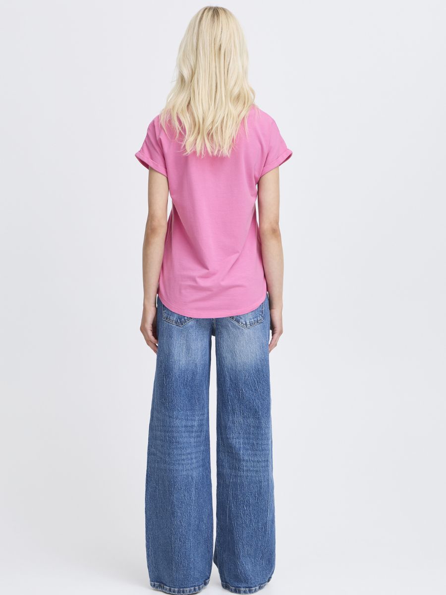 Person with long blonde hair wearing a bright pink short sleeve top and wide-leg blue denim jeans standing with back facing the camera