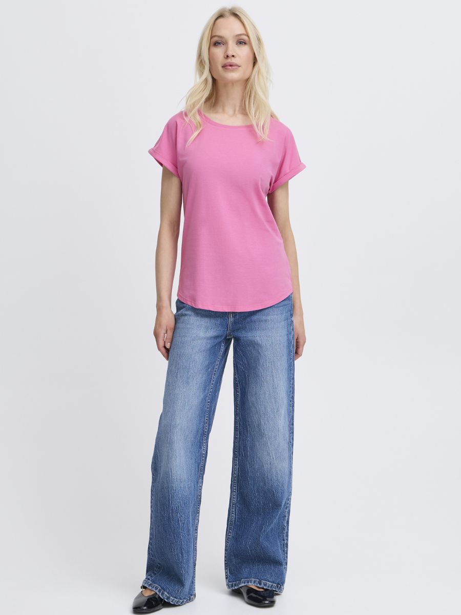 Person wearing a bright pink short-sleeve top paired with wide-leg blue denim jeans and black shoes.