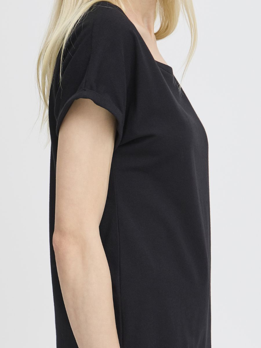 Side view of a person wearing a plain black short-sleeve top with a relaxed fit and cuffed sleeves