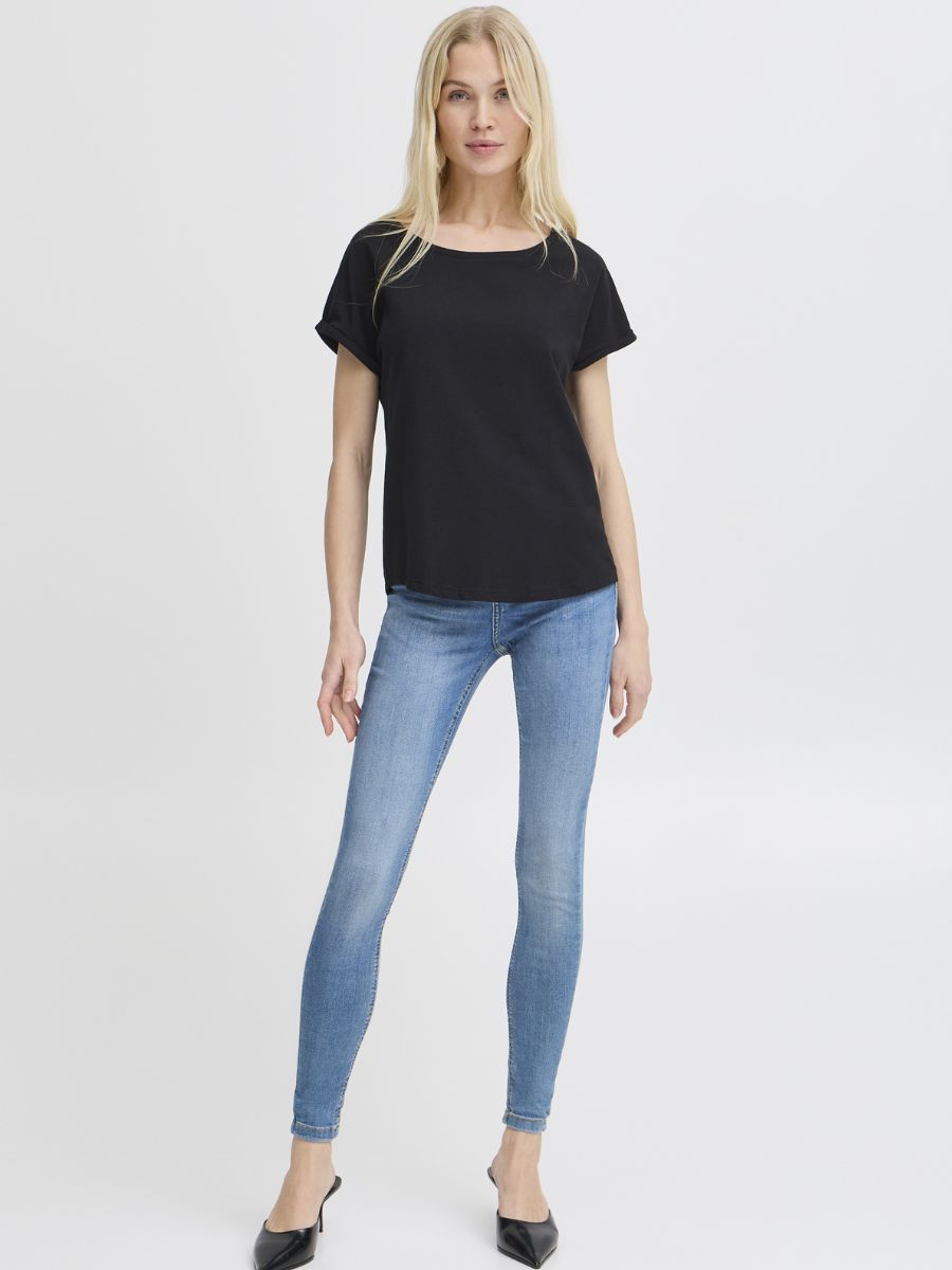 Person in a black short-sleeve top and light blue skinny jeans standing against a plain white background