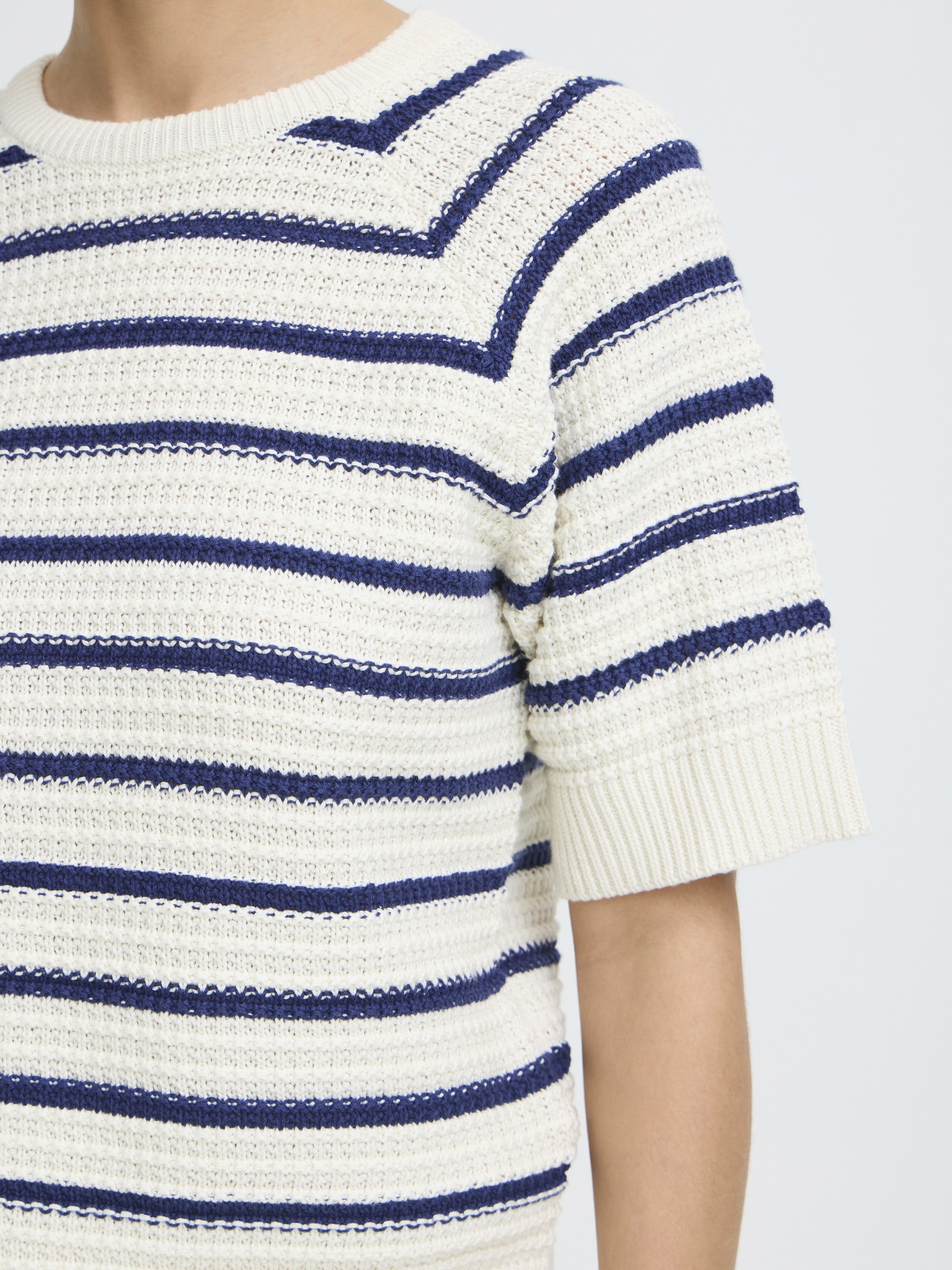 Close-up of a cream knit sweater with navy blue horizontal stripes and short ribbed sleeves.