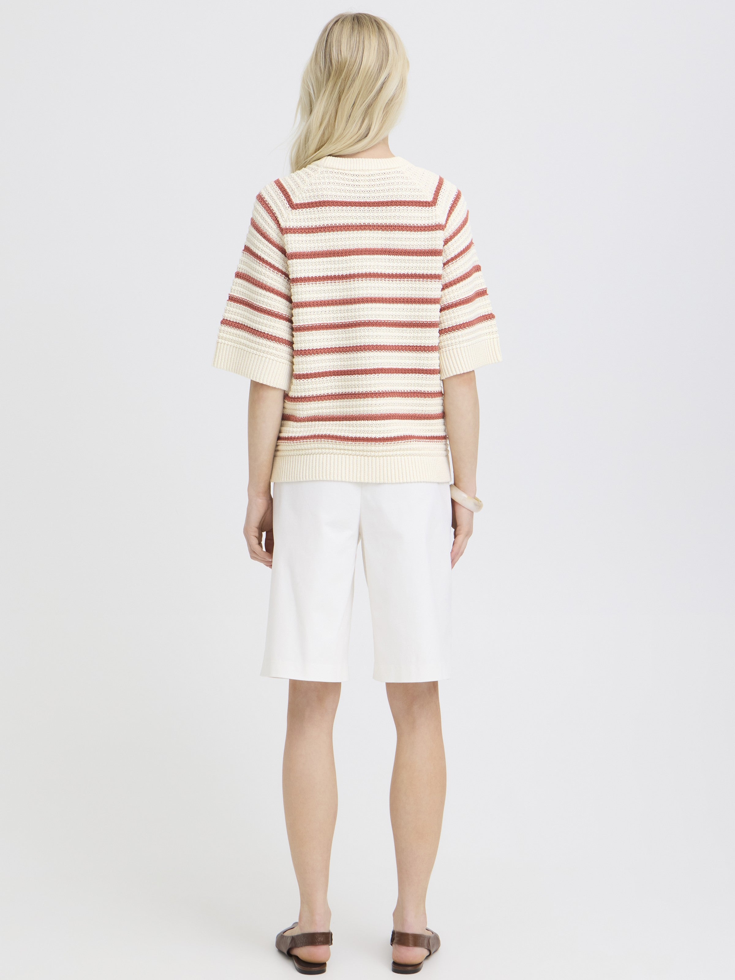 Person with long blonde hair wearing a cream and rust striped short-sleeve sweater and white knee-length shorts.