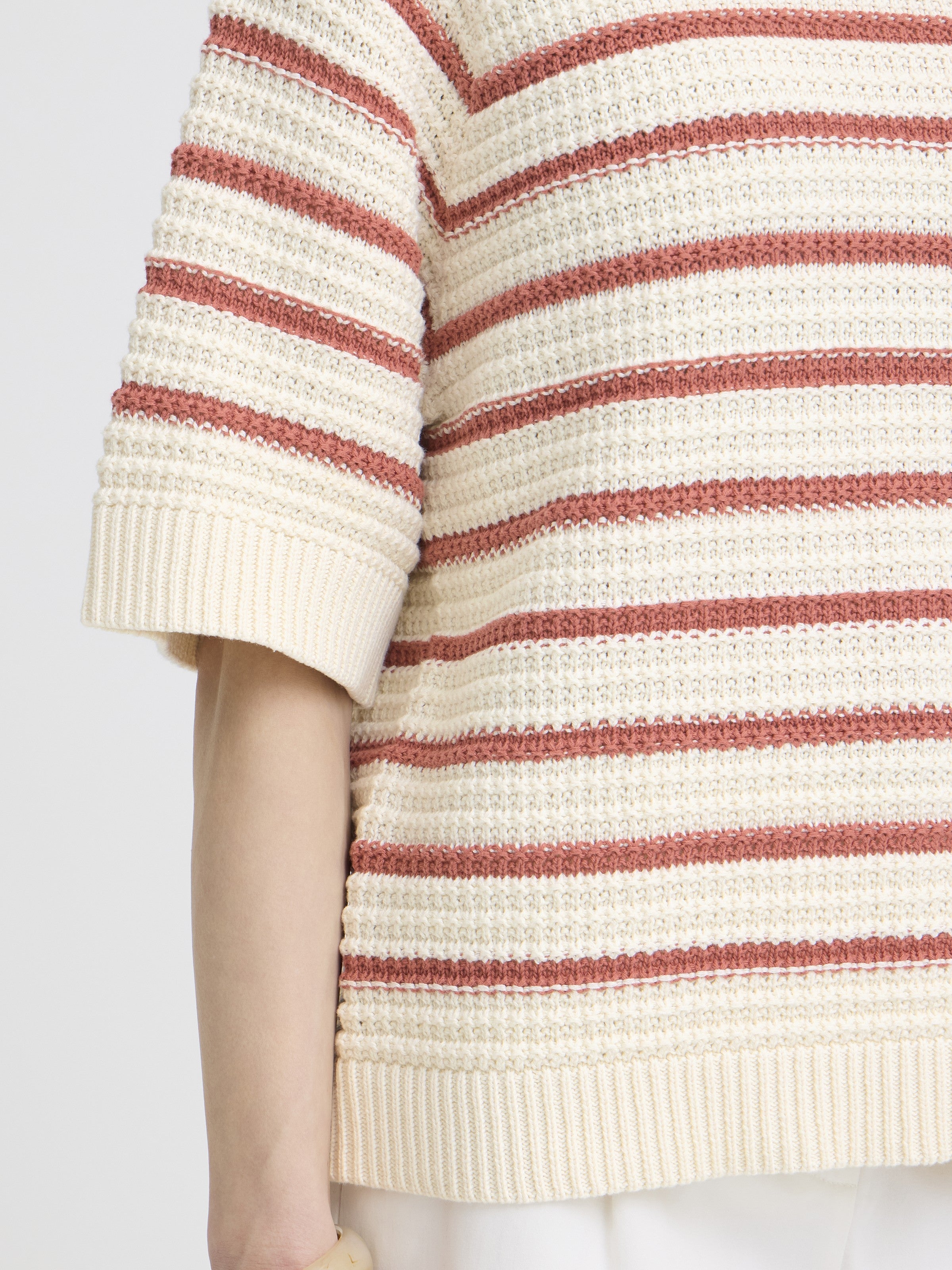 Close-up of a textured knit top with cream and rust-colored horizontal stripes and short sleeves.