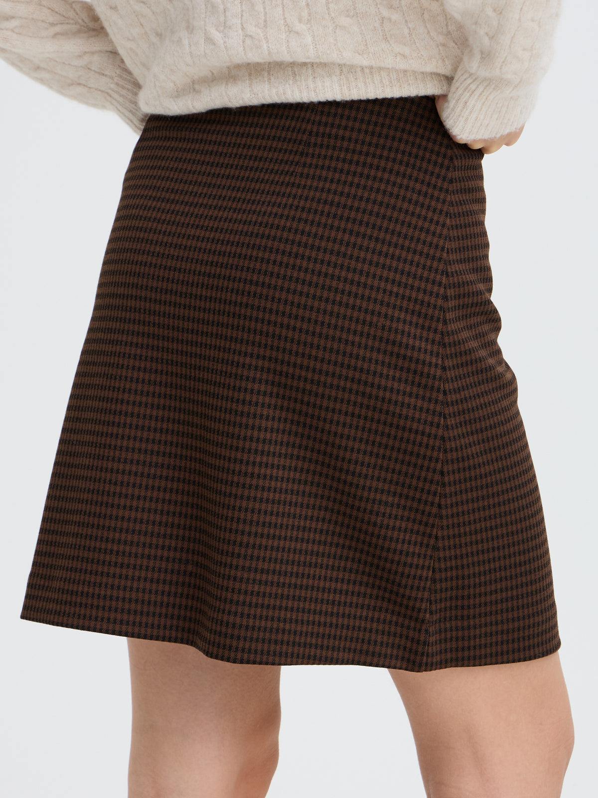 Brown and black checkered A-line skirt paired with a cream cable-knit sweater.