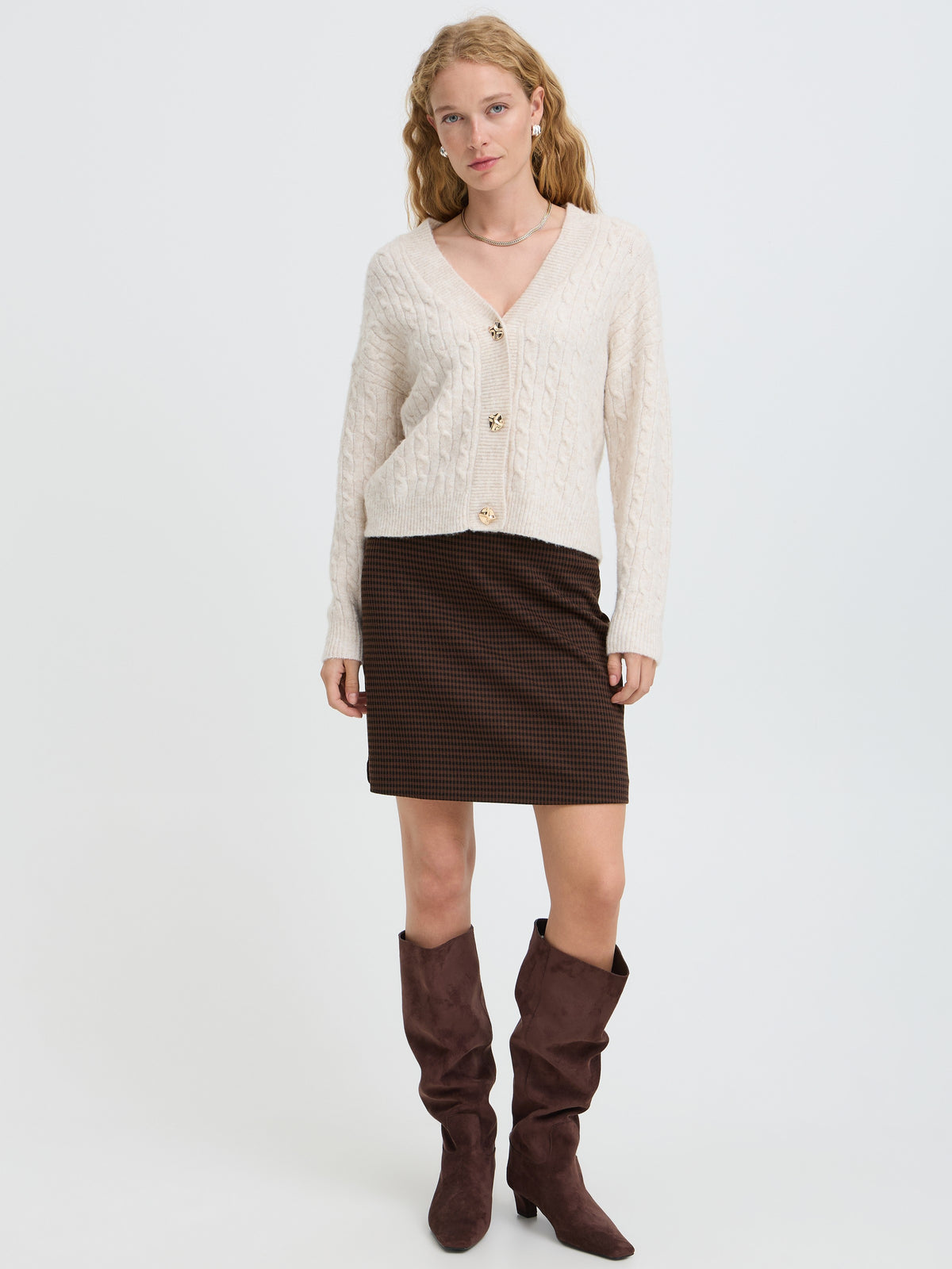 Cream cable knit cardigan with large buttons paired with a dark brown textured mini skirt and slouchy boots