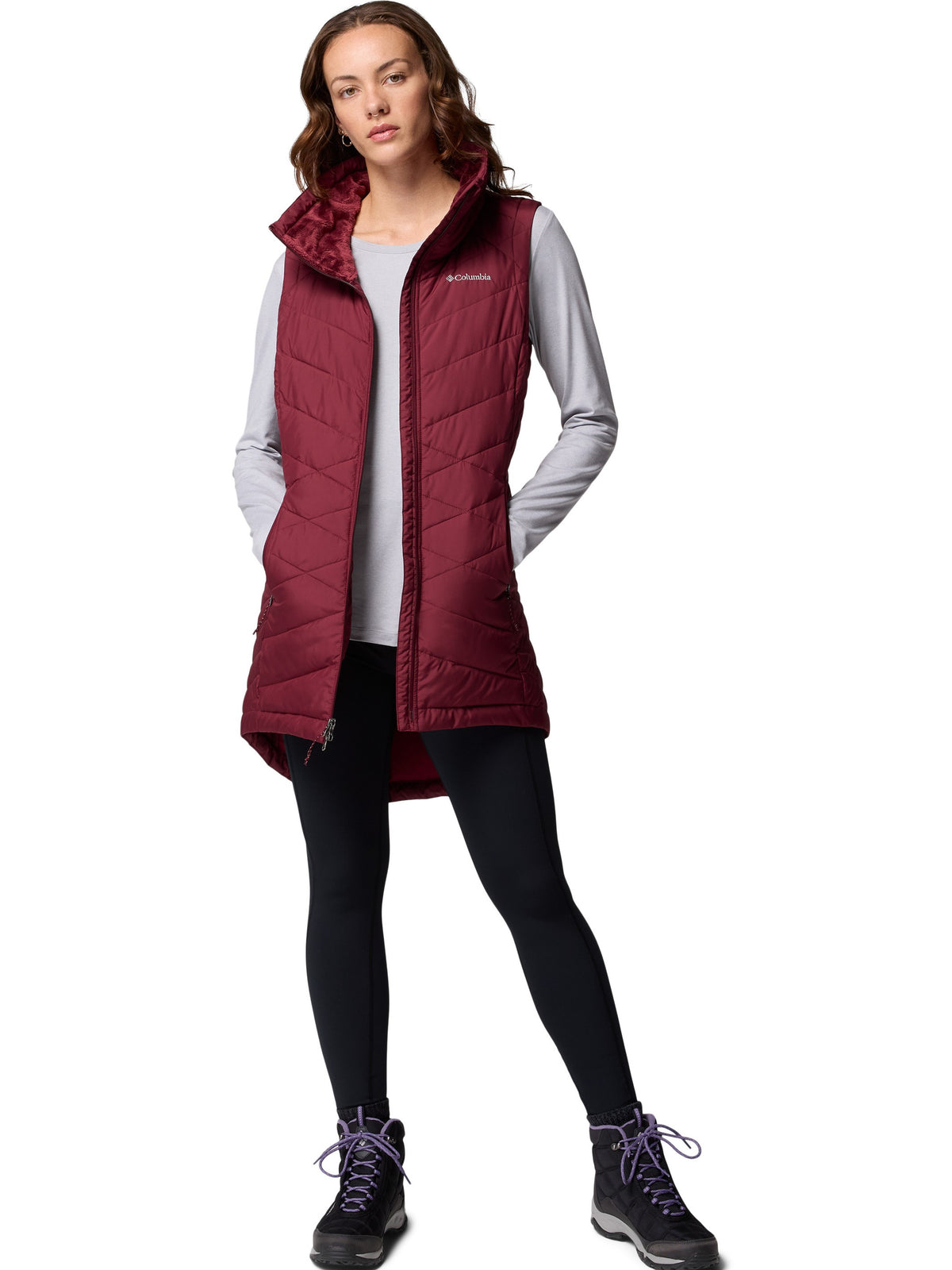 Columbia Heavenly II Omni-Heat Long Vest in deep red, styled with black leggings and hiking boots for outdoor warmth.