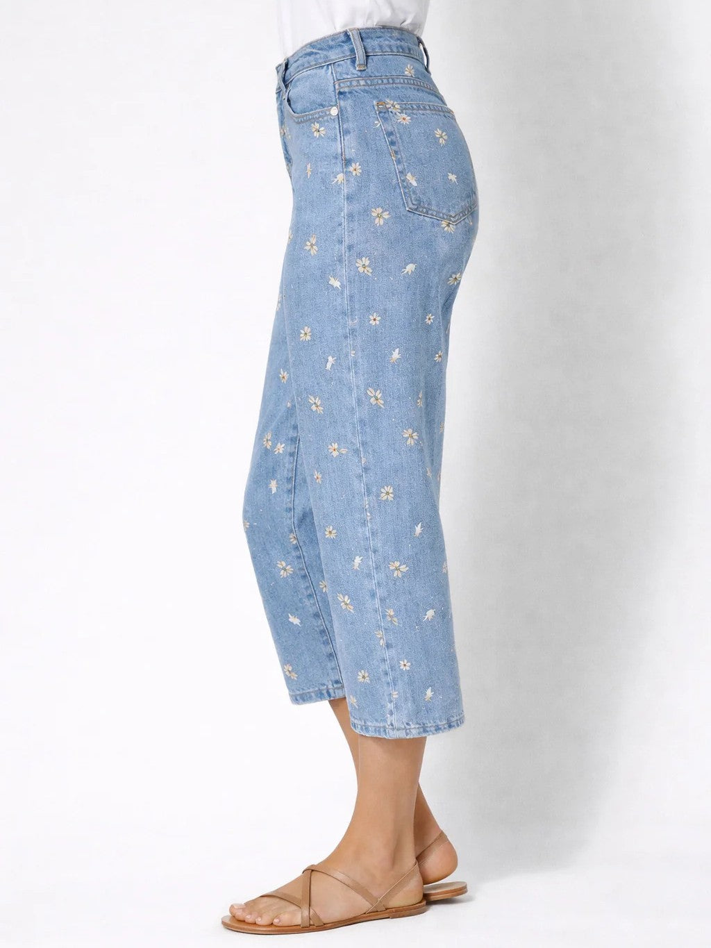 Light blue denim cropped pants with small white and yellow floral prints paired with tan flat sandals.