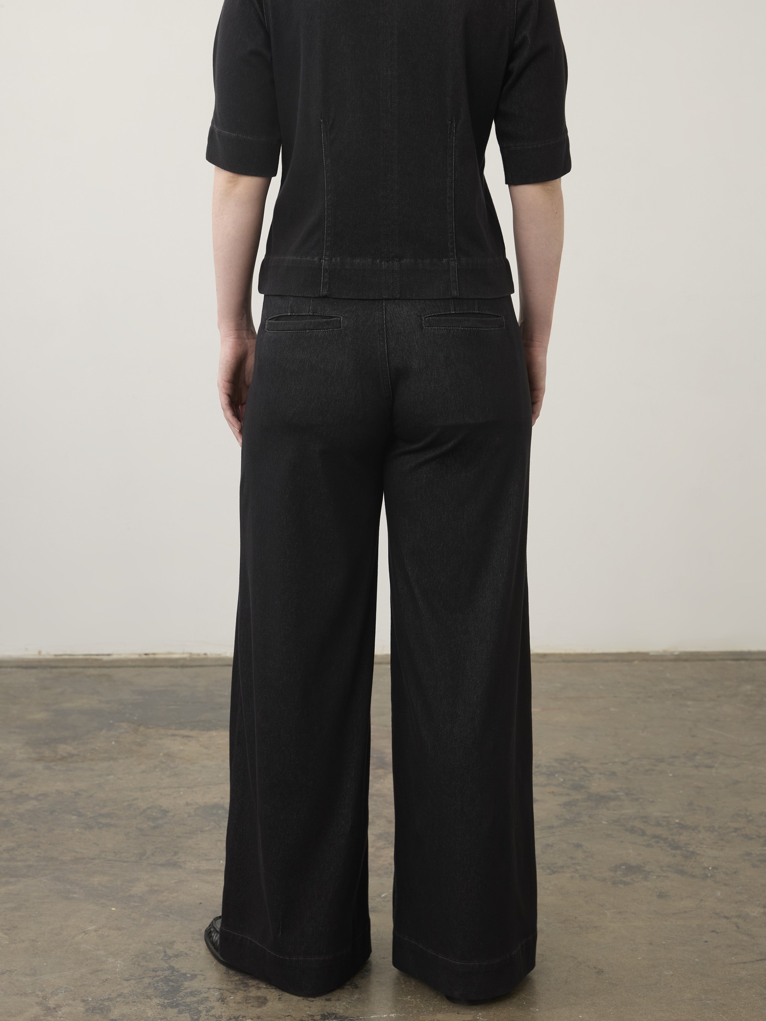 Back view of a black denim wide-leg pant and matching black top with elbow-length sleeves on a neutral background.