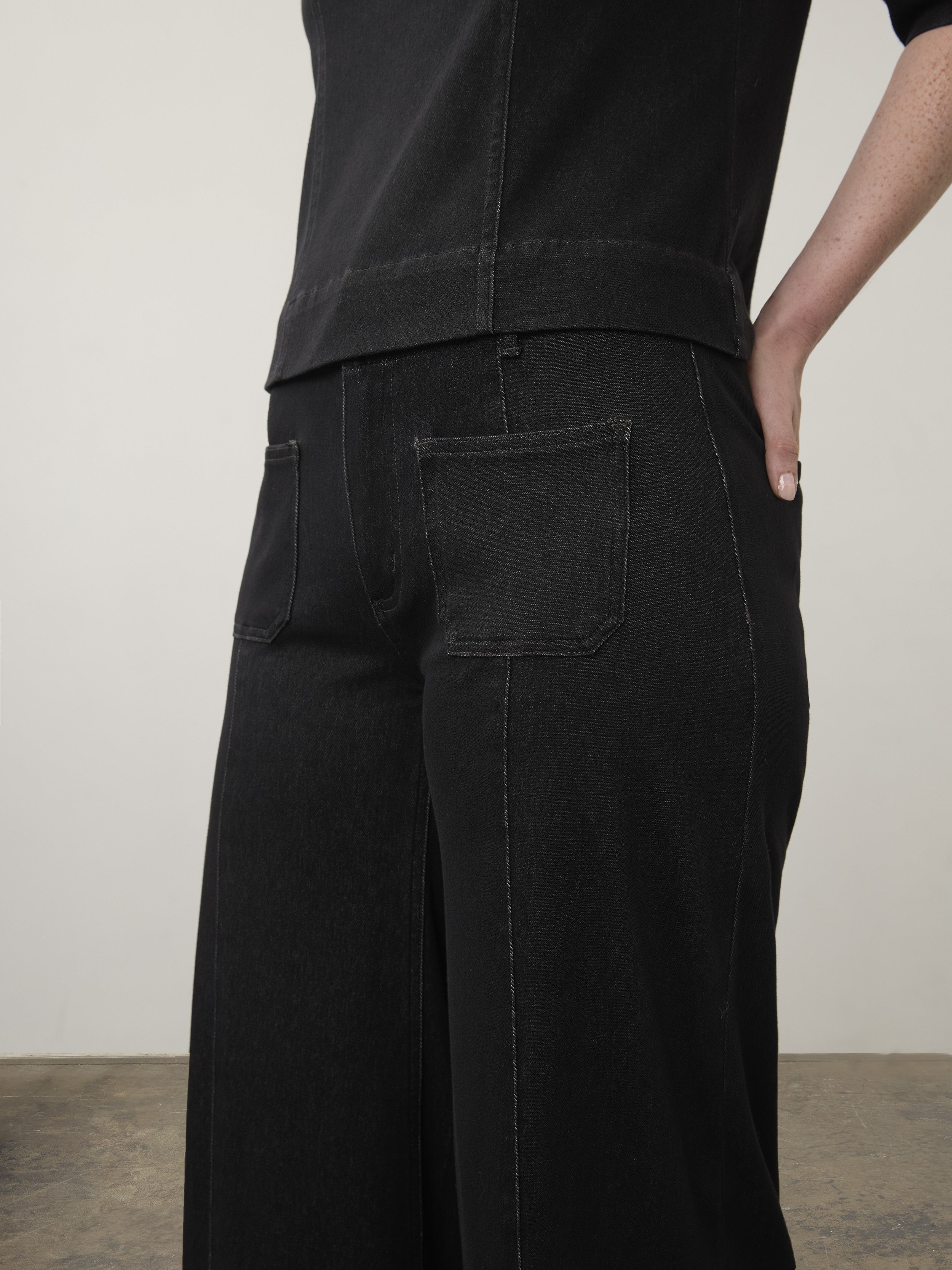Black wide-leg denim pants with large back pockets and visible stitching on a neutral background.