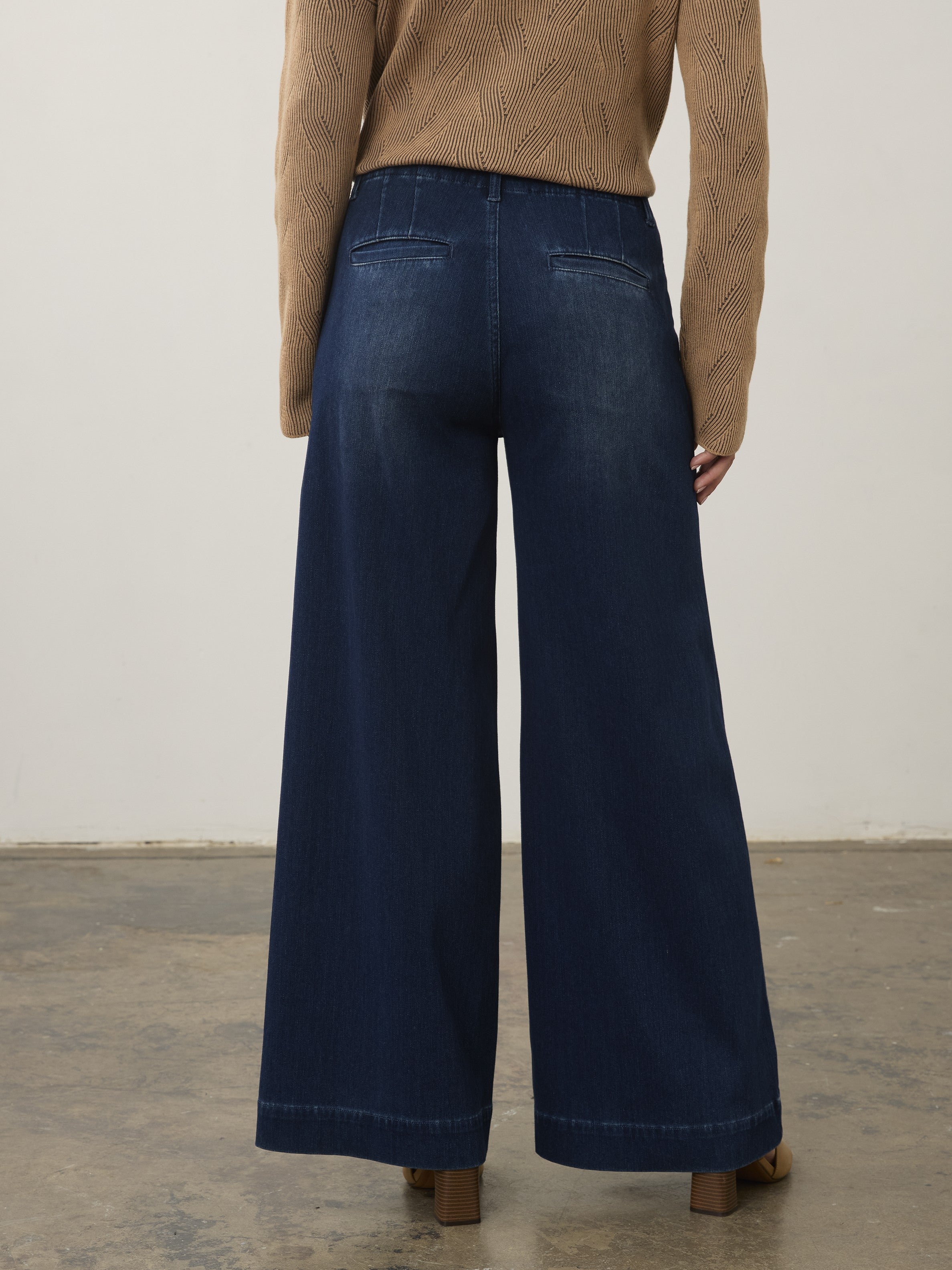 Back view of wide-leg dark denim pants paired with a textured brown long-sleeve top on a neutral background.