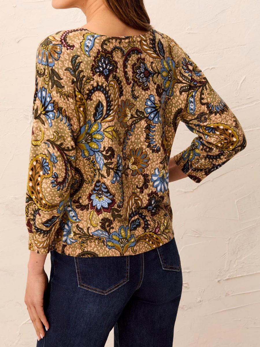 Floral patterned 3/4 sleeve top in earth tones paired with dark blue denim jeans against a textured wall background.