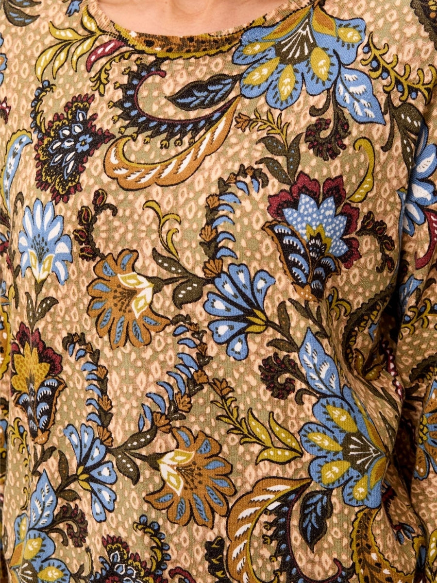Close-up of a fabric with a detailed floral pattern in blue, brown, green, and mustard tones on a beige background.
