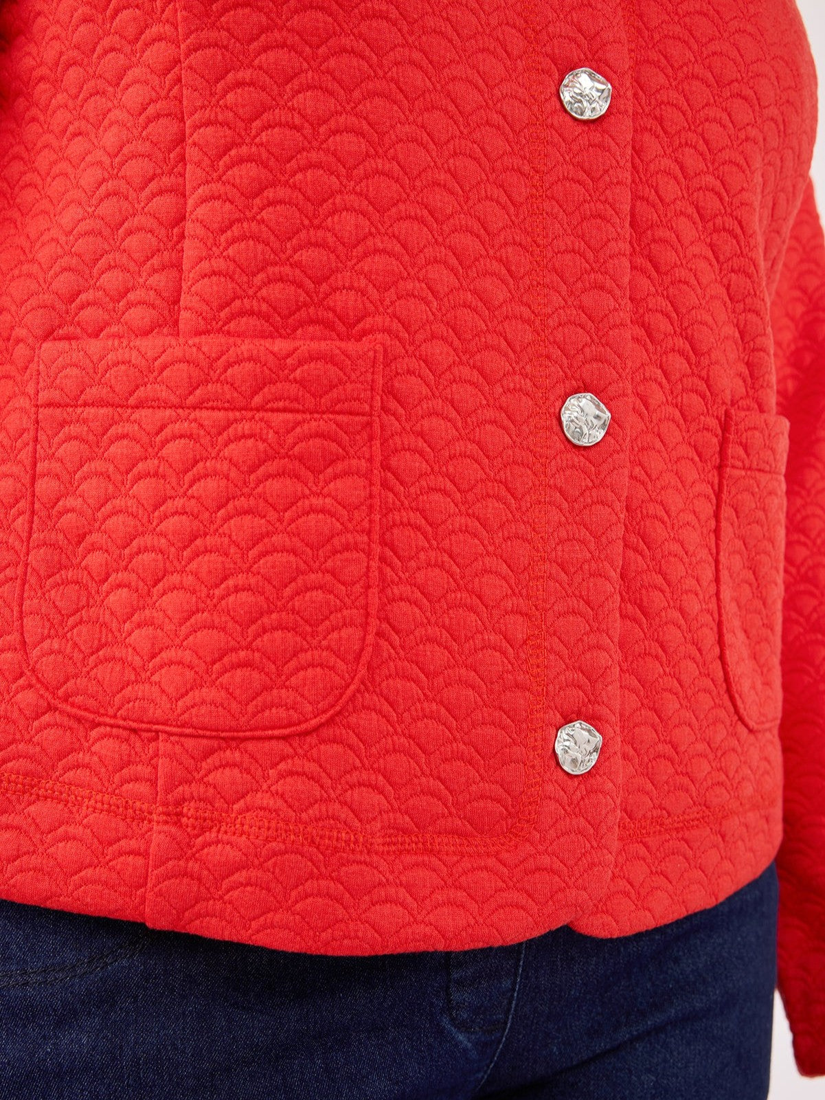 Close-up of a red textured jacket with scalloped pattern, silver snap buttons, and front patch pockets.
