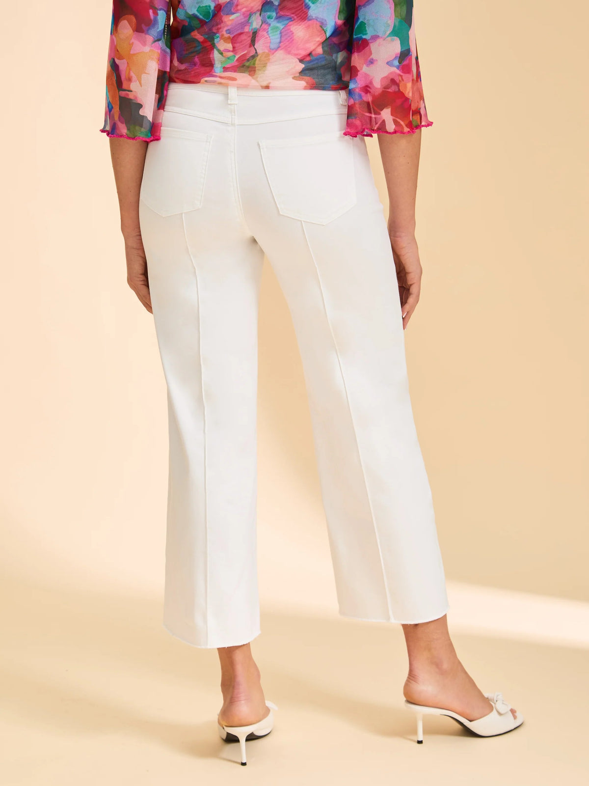 Rear view of white cropped pants with back pockets paired with floral sheer top and white heeled mules.