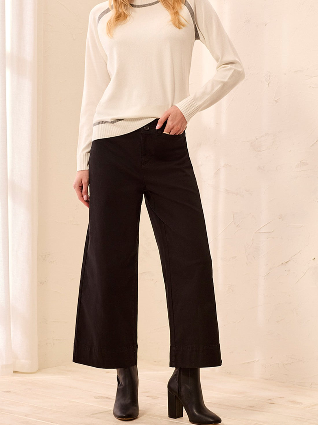 Black wide-leg pants paired with a cream long-sleeve sweater and black heeled ankle boots.