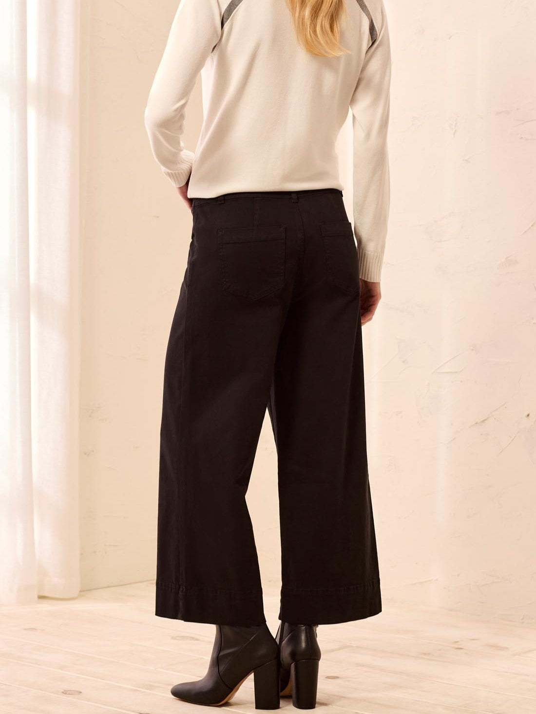 Back view of wide-leg black pants paired with black heeled ankle boots and a cream long-sleeve top.