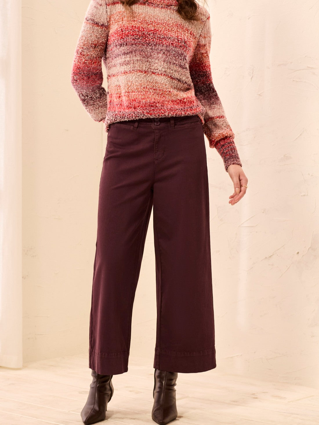 Multicolored knit sweater paired with high-waisted wide-leg burgundy pants and black heeled boots.