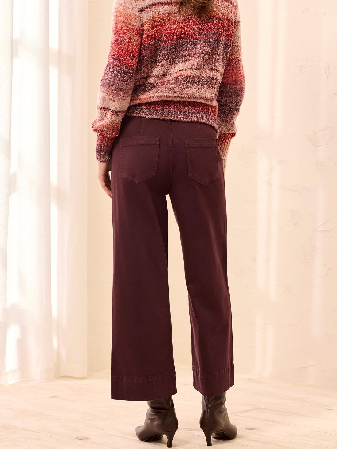 Back view of a person wearing wide-leg brown pants paired with a multicolored knit sweater and brown heeled boots.
