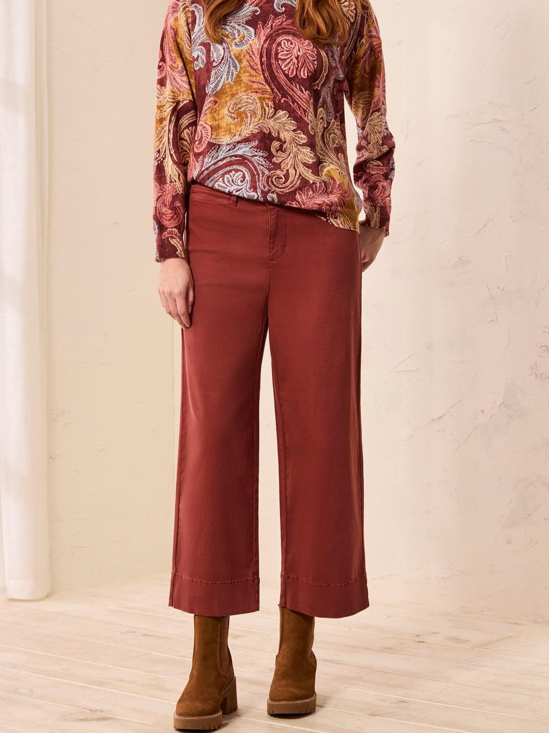 Red wide-leg cropped pants paired with brown suede ankle boots and a paisley patterned long-sleeve top