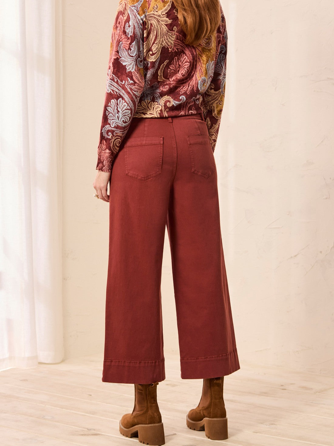 Wide-leg cropped pants in a deep paprika color paired with brown heeled ankle boots against a neutral background.