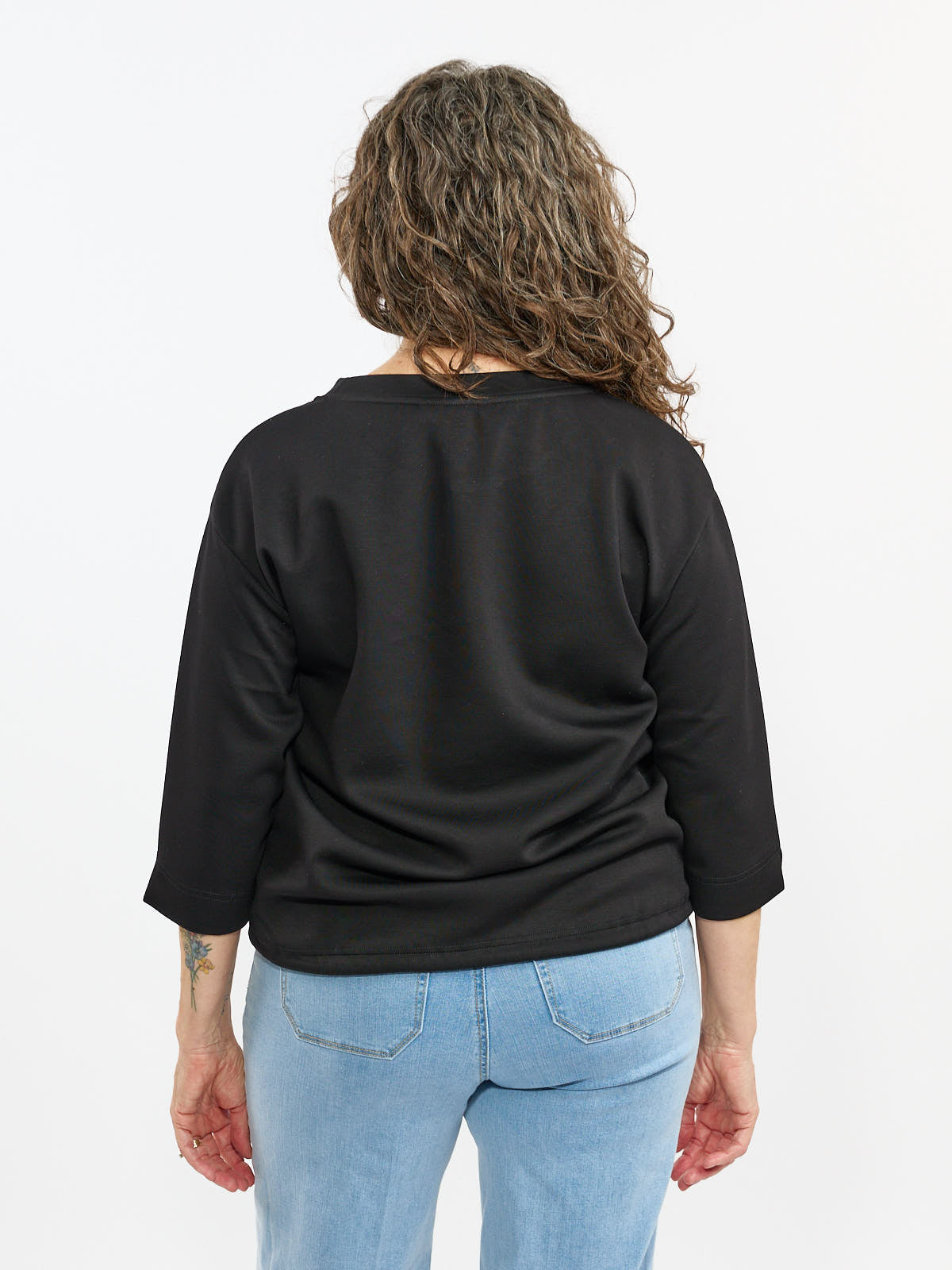 Back view of a black long-sleeve top paired with light blue denim jeans on a white background.