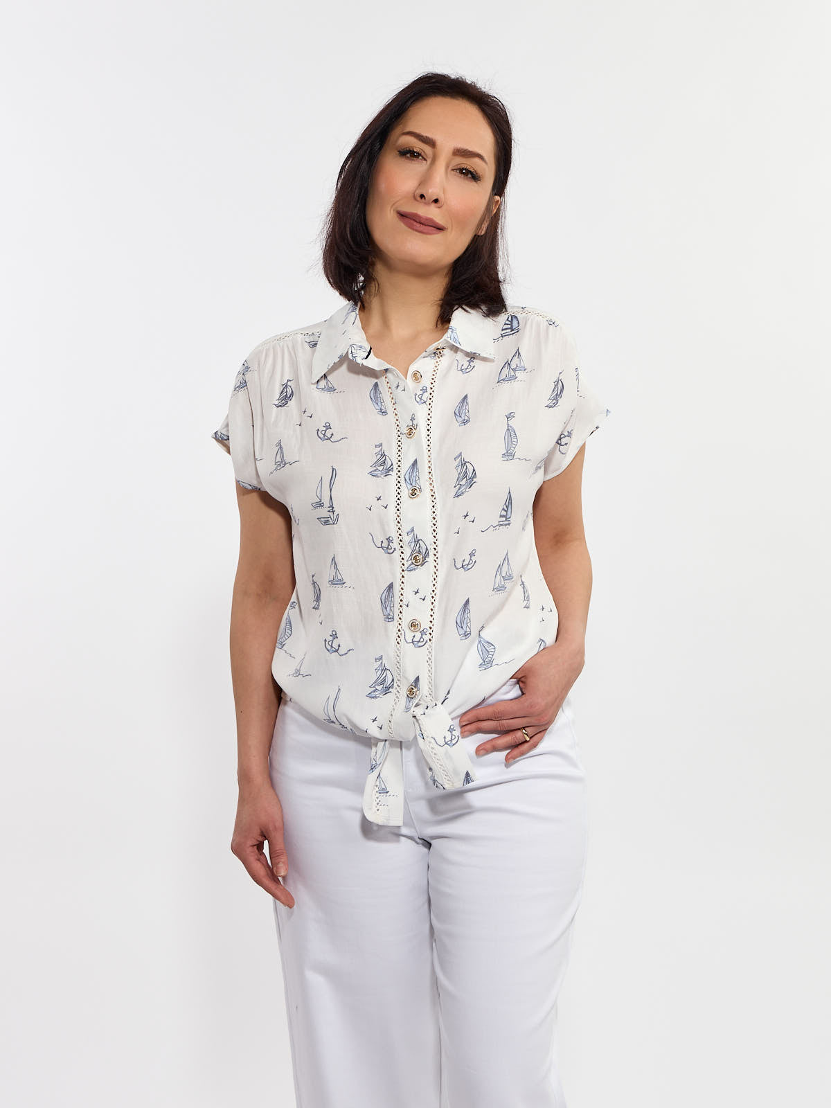 Short-sleeve white blouse with blue nautical prints and front tie, paired with white pants on light background.