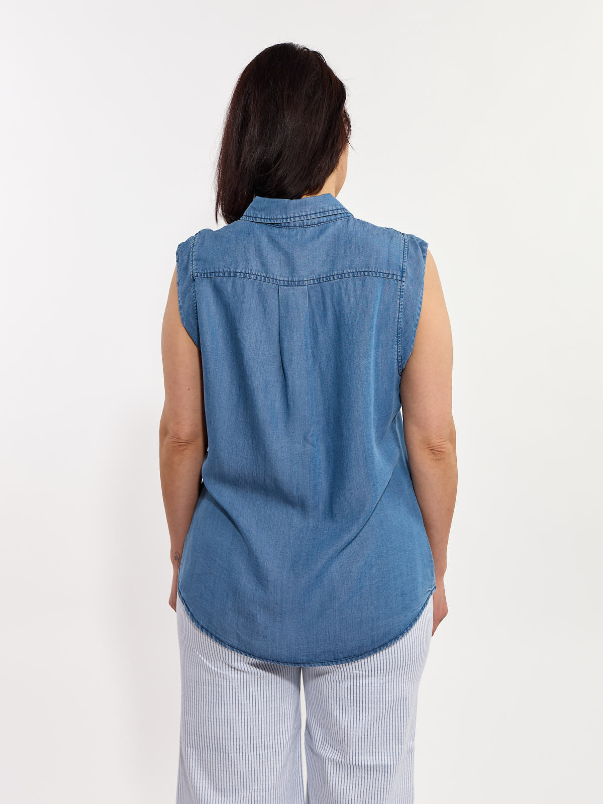 Back view of a sleeveless blue denim top paired with light-colored striped pants against a plain background.