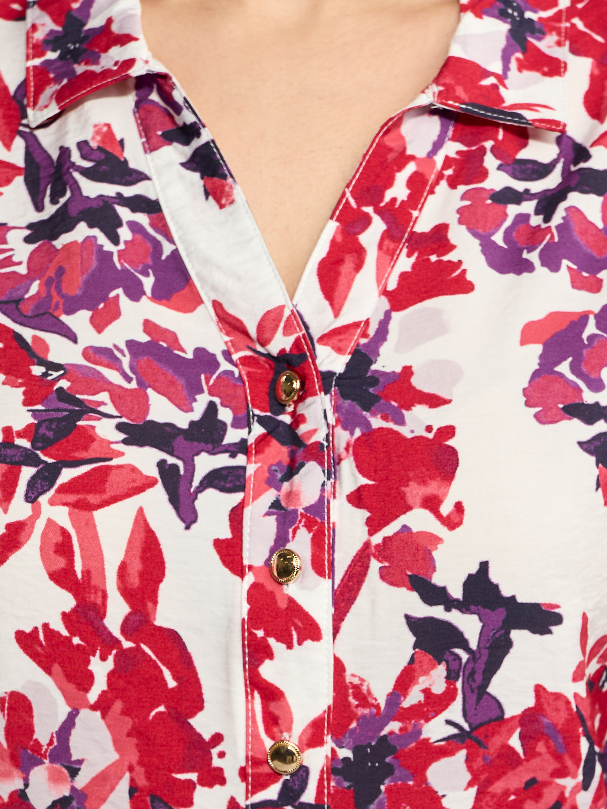 Close-up of a floral patterned top with red, purple, and black abstract prints and gold buttons on a white background.
