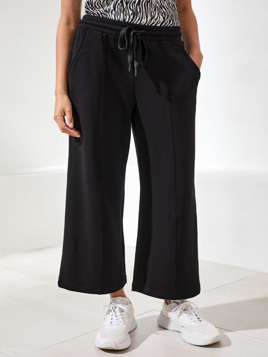Tribal Techno Lux Tie-Waist Crop 26" Pants in black by Tribal Sportswear Inc. styled with white sneakers.