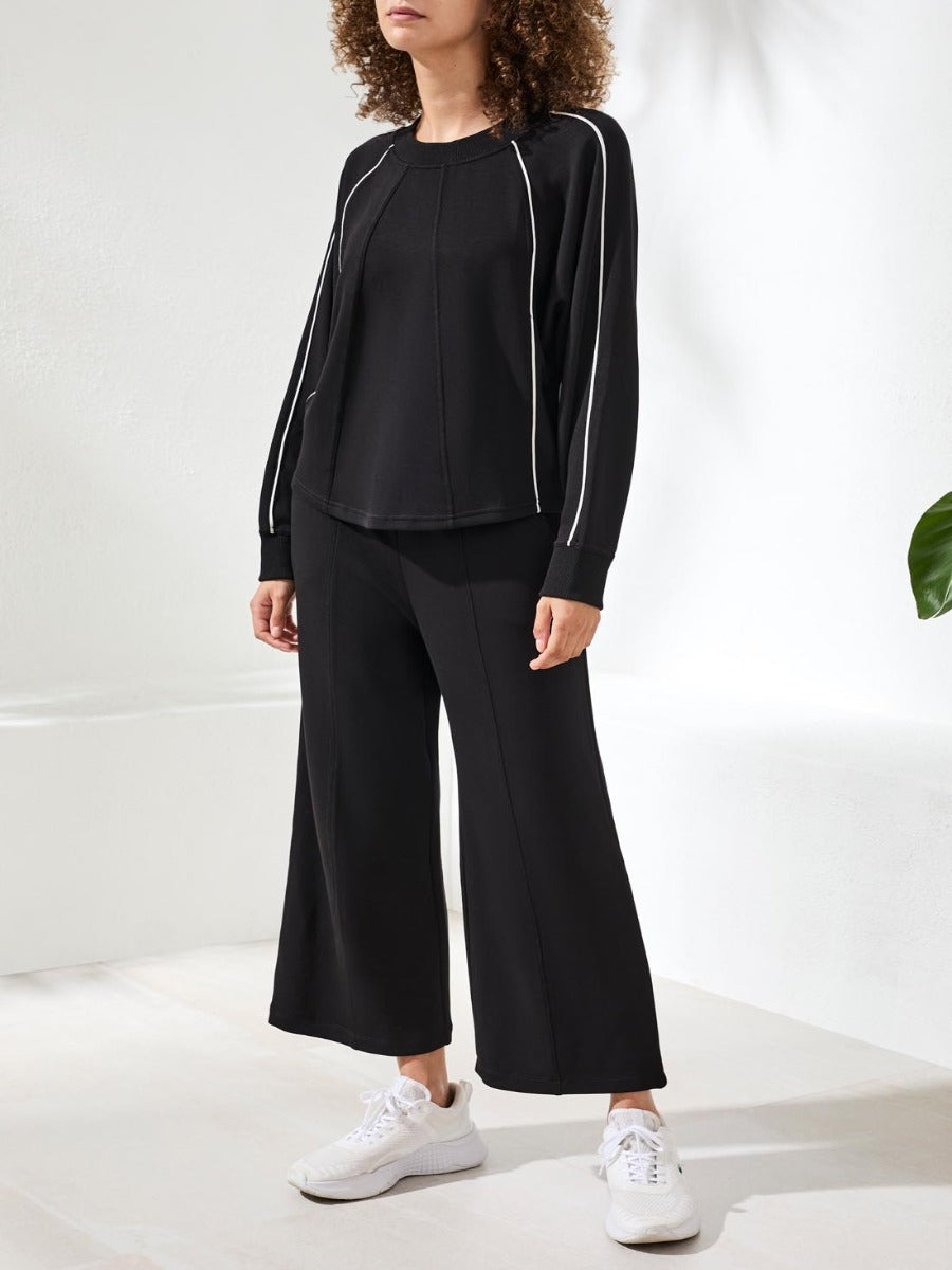 Black long sleeve top with white piping detail paired with wide-leg black pants and white sneakers