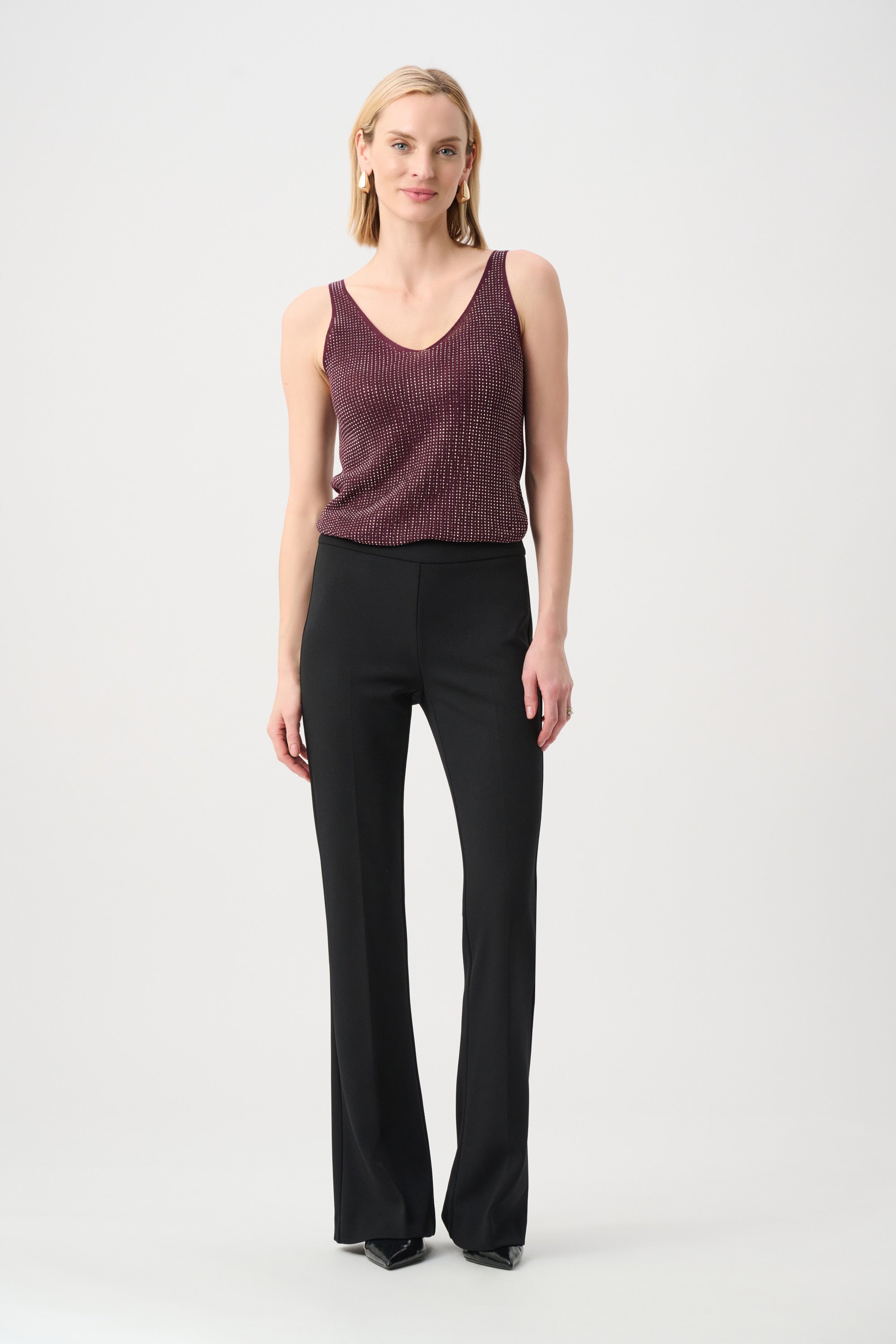 Sleeveless knit top in dark berry paired with high-waisted black trousers and black pointed shoes on light background.