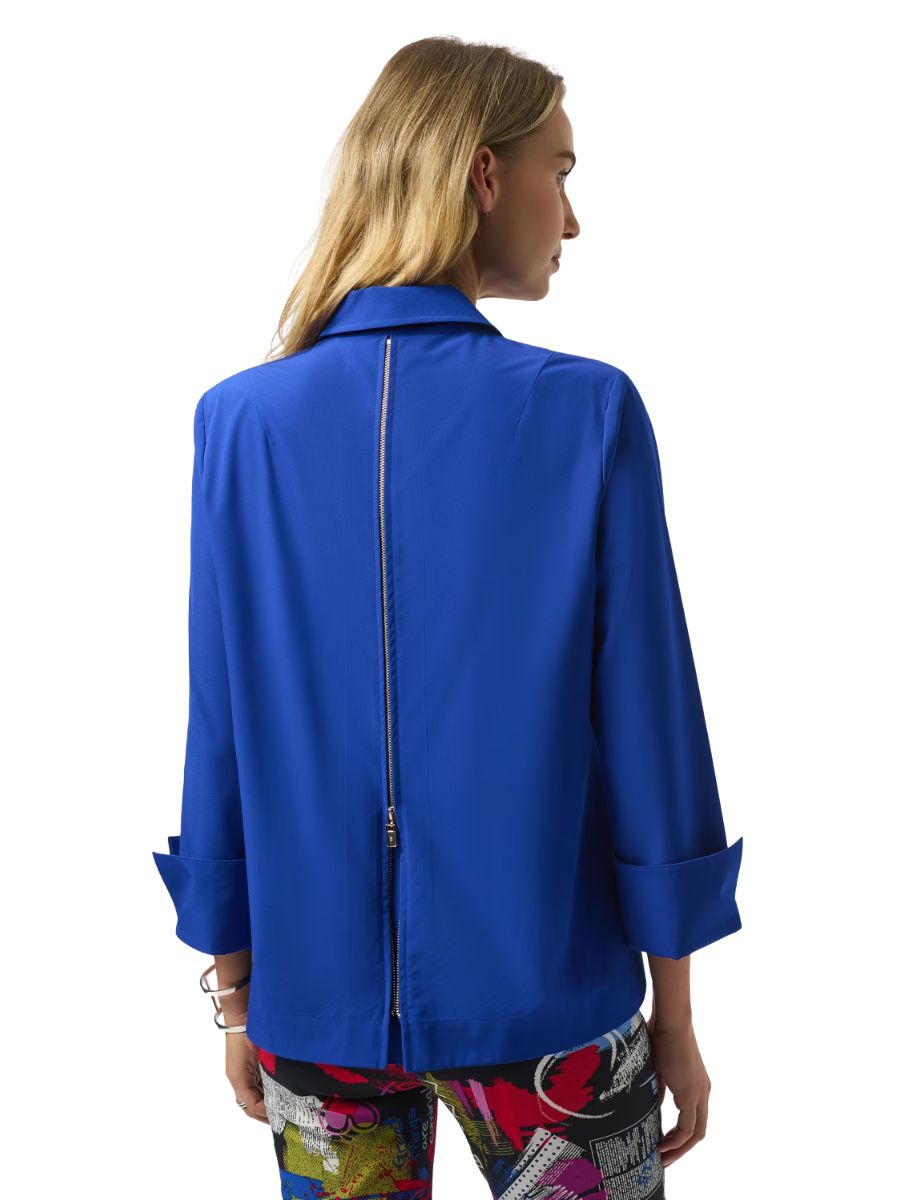 Back view of a person wearing a vibrant blue jacket with a central zipper detail and colorful patterned pants.