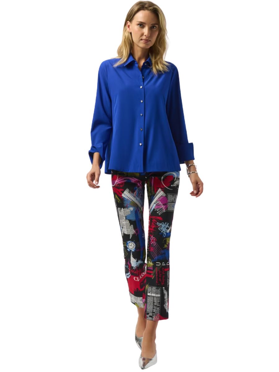 Person in a bright blue button-up shirt and colorful abstract print cropped pants walking in silver heels.