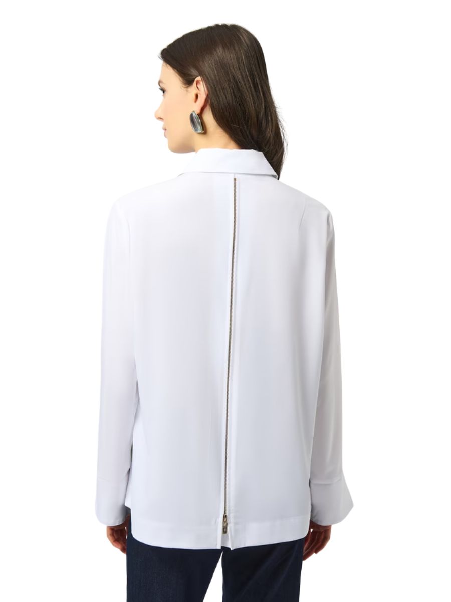 Back view of a white long-sleeve top with a central zipper detail, worn with dark pants and geometric earrings.