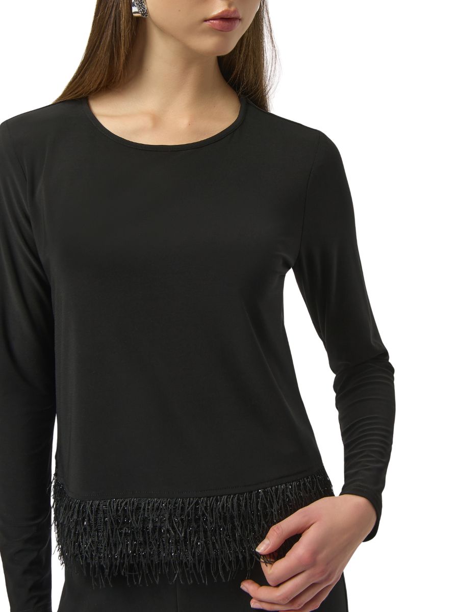 Close-up of a black long-sleeve top with a fringe detail along the hem worn by a person